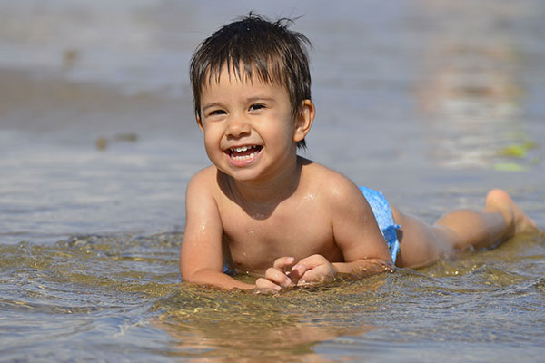 Child laying on beach in water - find out everything you need to know about SPF boosters in sunscreen formulations in the Prospector Knowledge Center.