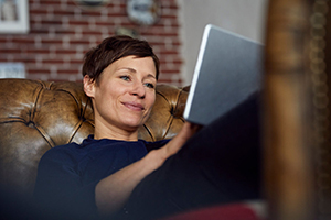 Woamn sitting on sofa at home, using digital tablet