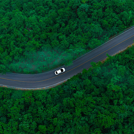 Aerial view of dark green forest road and white electric car Natural landscape and elevated roads Adventure travel and transportation and environmental protection concept