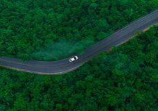 Aerial view of dark green forest road and white electric car Natural landscape and elevated roads Adventure travel and transportation and environmental protection concept