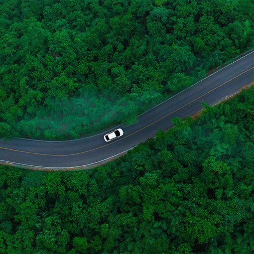 Aerial view of dark green forest road and white electric car Natural landscape and elevated roads Adventure travel and transportation and environmental protection concept