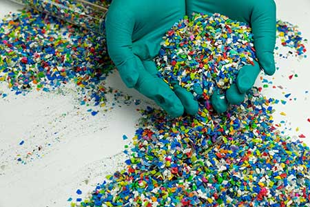 Two gloved hands holding plastic pellets