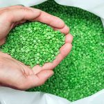 Hands scooping up green biodegradable plastic pellets
