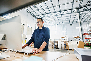 Medium shot of male warehouse worker checking orders at computer work station in warehouse