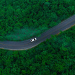 Aerial view of dark green forest road and white electric car Natural landscape and elevated roads Adventure travel and transportation and environmental protection concept