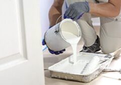 Man pours paint into the tray and dips roller. Professional interior construction worker pouring white color paint to tray.
