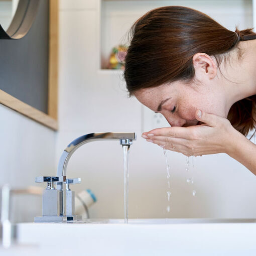Young woman refreshing her face with water in bathroom